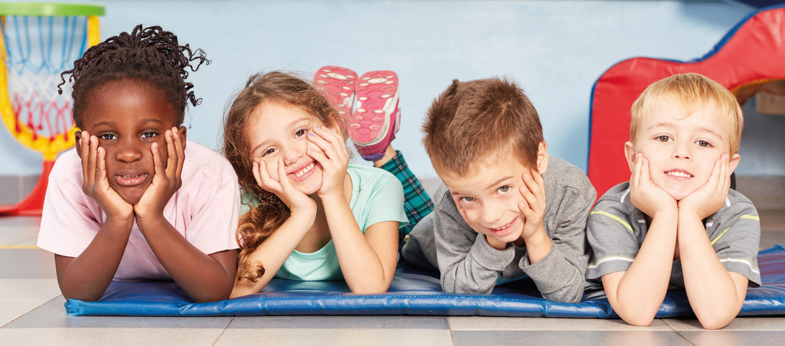 Vier Kinder liegen nebeneinander auf einer Matratze und lächeln in die Kamera