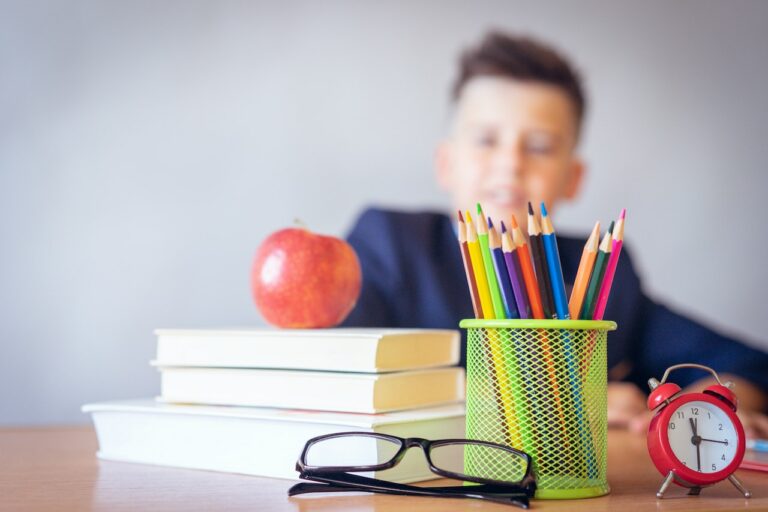 Bücher, Stifte, eine Brille und ein Apfel auf einem Tisch - dahinter ein Schulkind