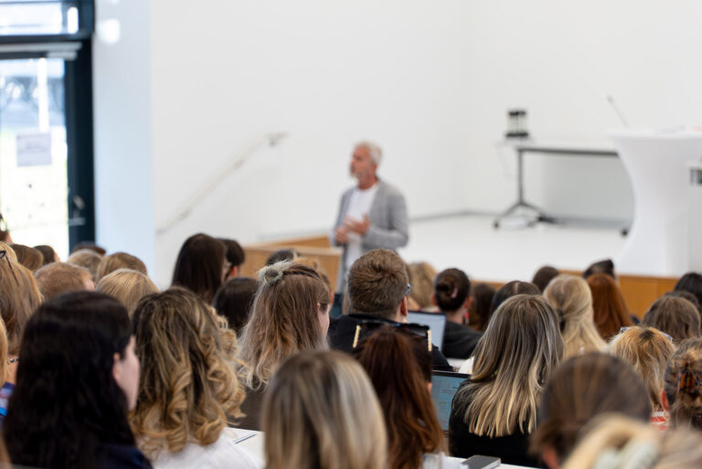Neulehrer*innen im vollen Audimax hören einem Vortragenden zu