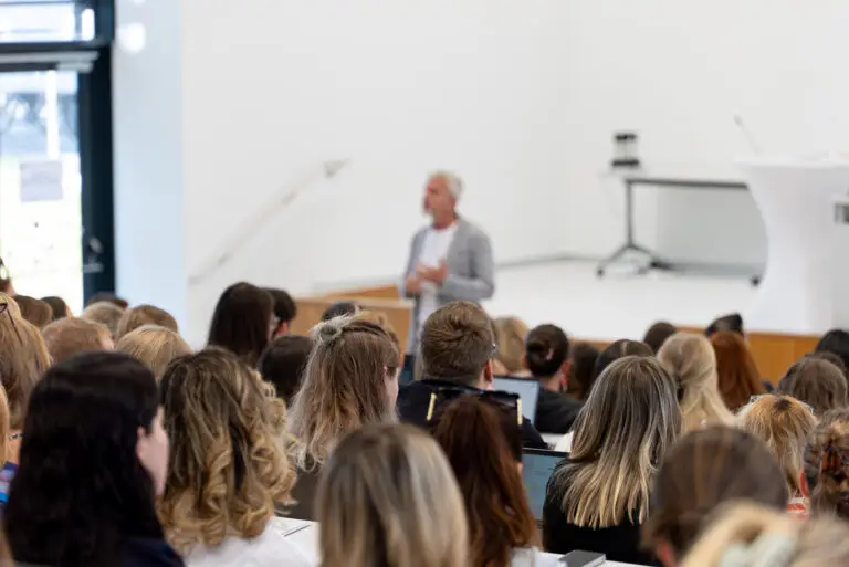 Neulehrer*innen im vollen Audimax hören einem Vortragenden zu